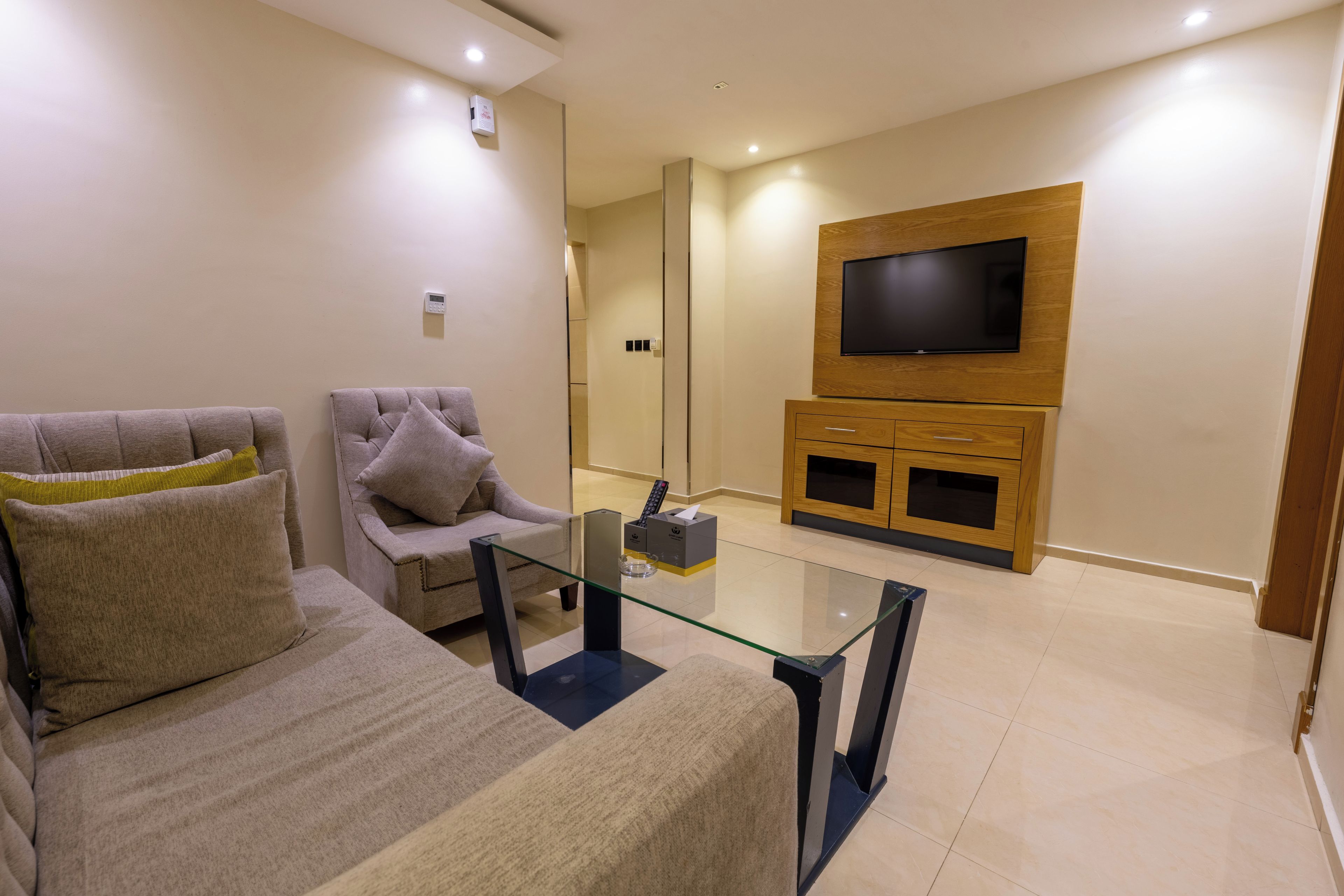 Una sala de estar moderna con sofá, sillón, mesa de centro de vidrio, televisor y mueble de entretenimiento de madera.