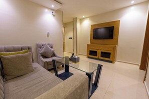A modern living room with a sofa, armchair, glass coffee table, TV, and wooden entertainment unit. - Al MuhaidbResidence Al Takhasossi 1 - Economic (Riyadh)