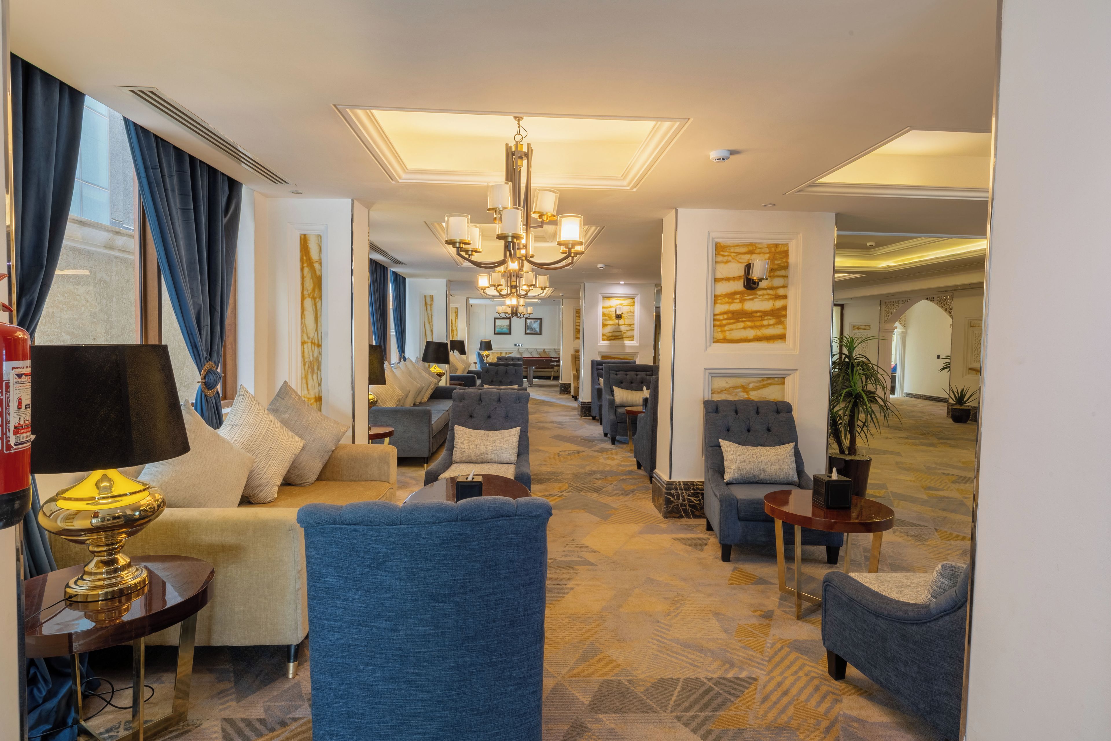 A hotel lobby with a long seating area, a chandelier, and a fire extinguisher.