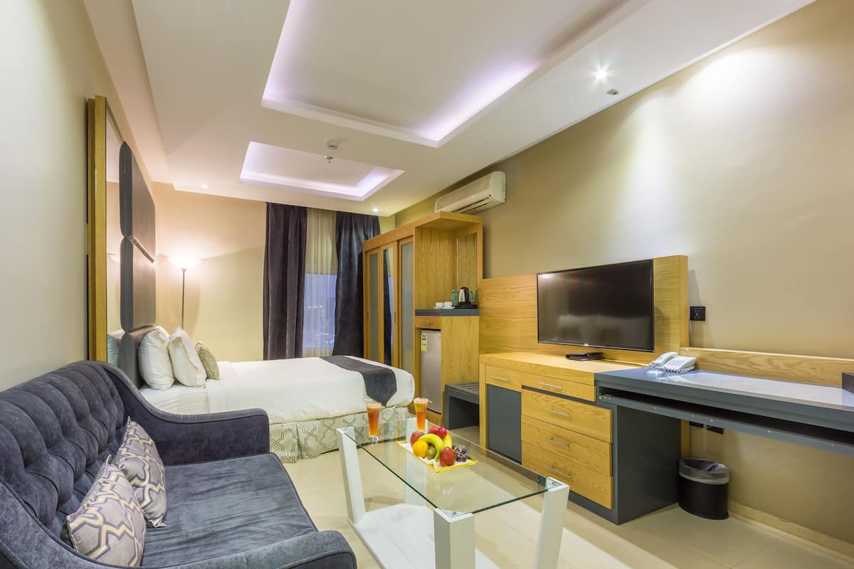 A modern hotel room with a bed, a sofa, a desk, and a TV.