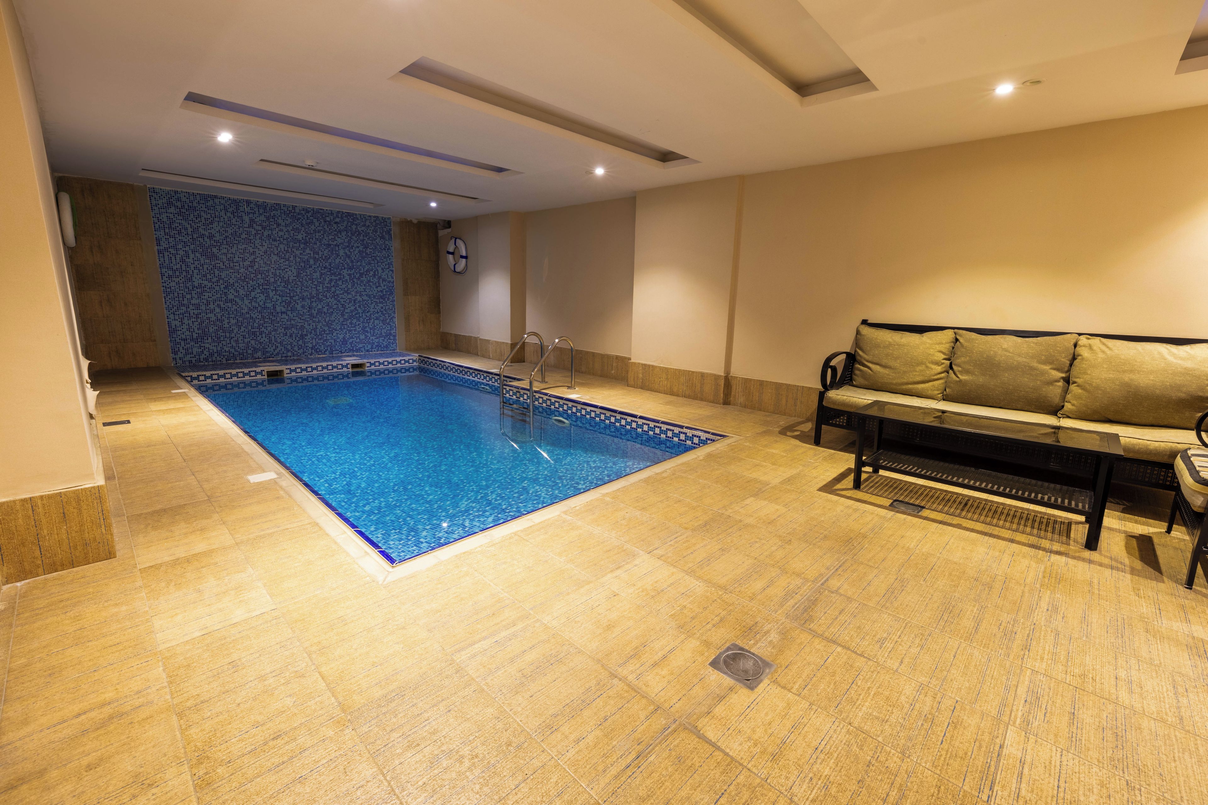 A swimming pool with a tiled edge, a sofa, and a coffee table in a room with a tiled floor and a wall with a blue pattern.