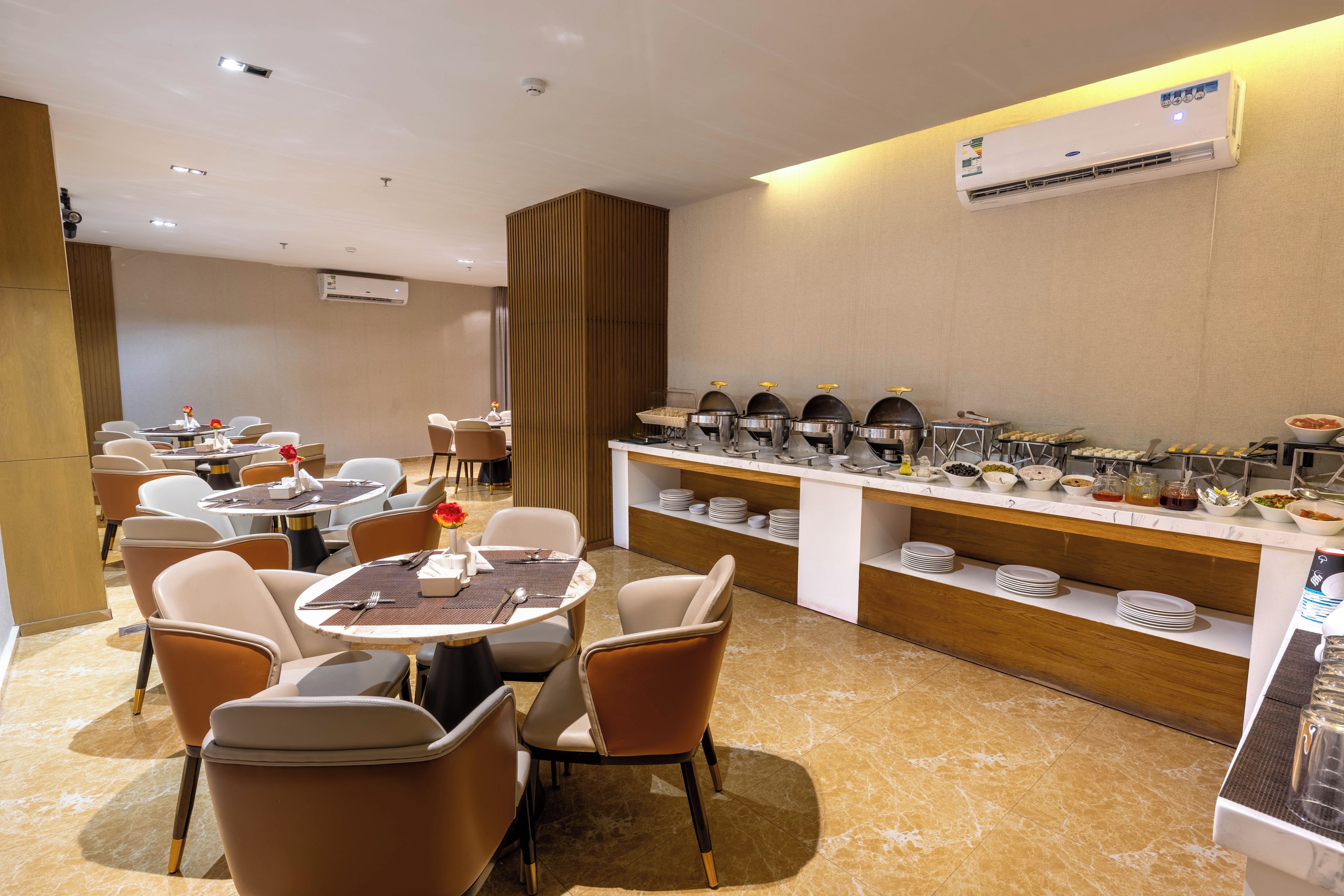 Un comedor moderno con mesas redondas, sillas y un mostrador tipo buffet.