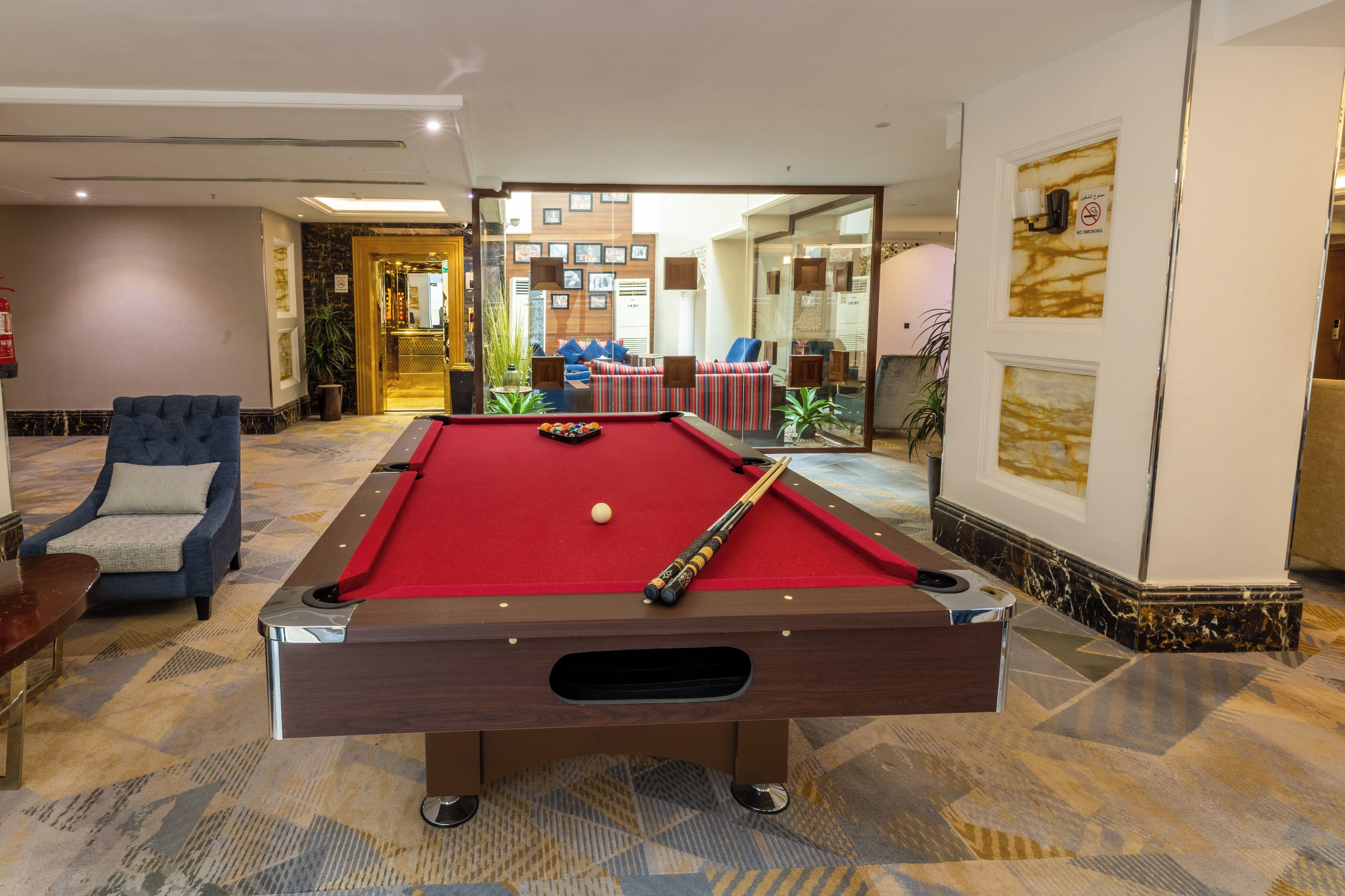 Una mesa de billar en el vestíbulo de un hotel con un sillón azul y un extintor.