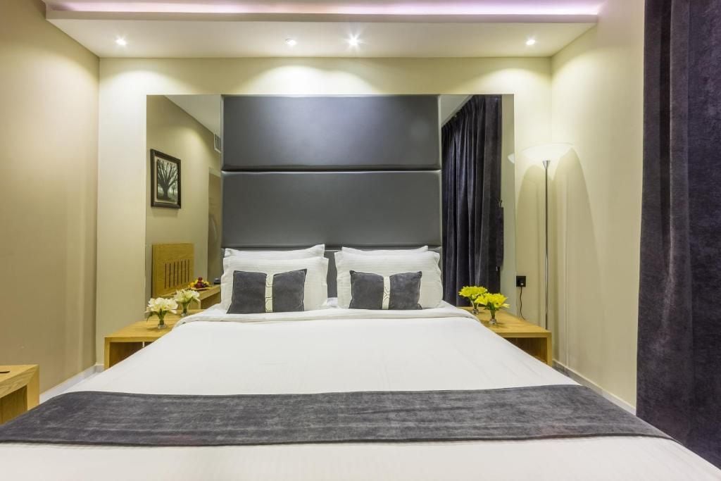 A hotel room with a large bed, bedside tables, a nightstand, a mirror, and a lamp.