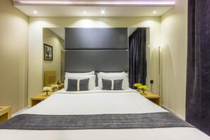 Una habitación de hotel con una cama grande, mesitas de noche, un espejo y una lámpara.