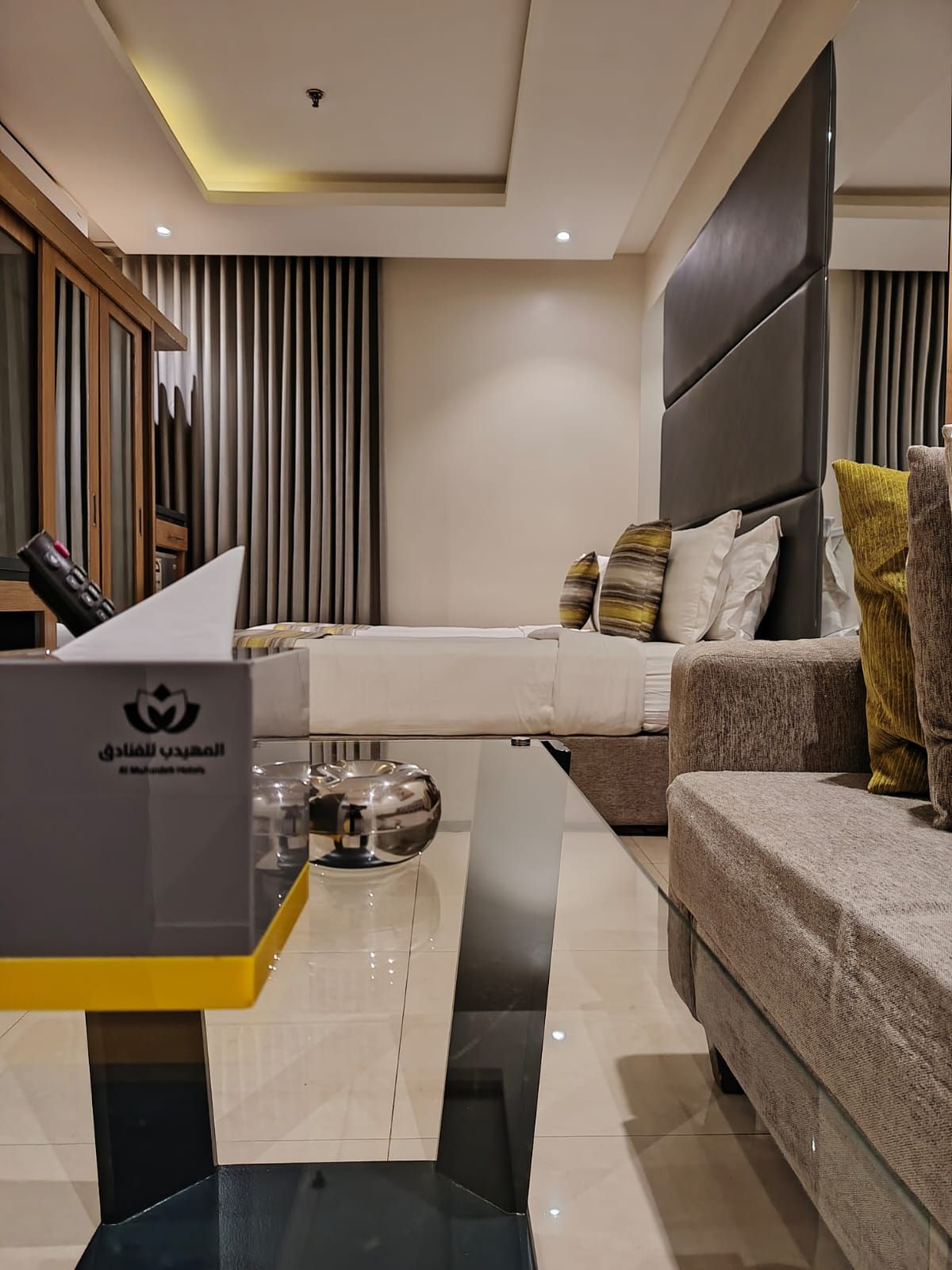 A modern living room with a sofa, a coffee table, and a bed with a headboard.
