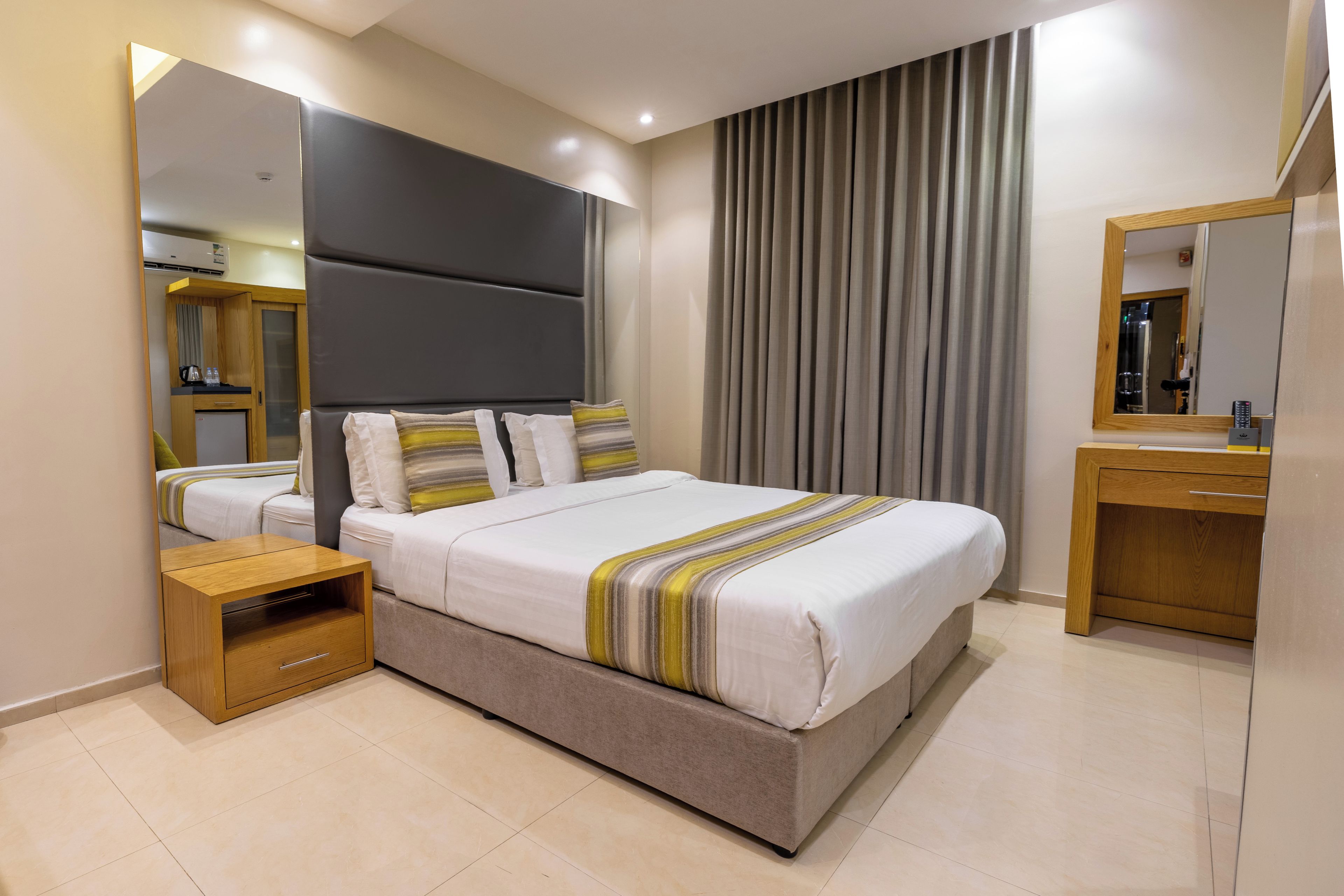 Una habitación de hotel moderna con una cama grande, una mesita de noche, un espejo y un armario.