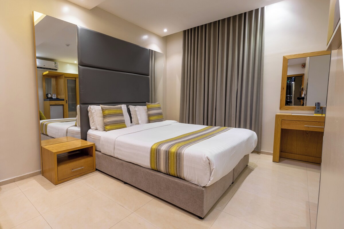 Una habitación de hotel moderna con una cama grande, una mesita de noche, un espejo y un armario.