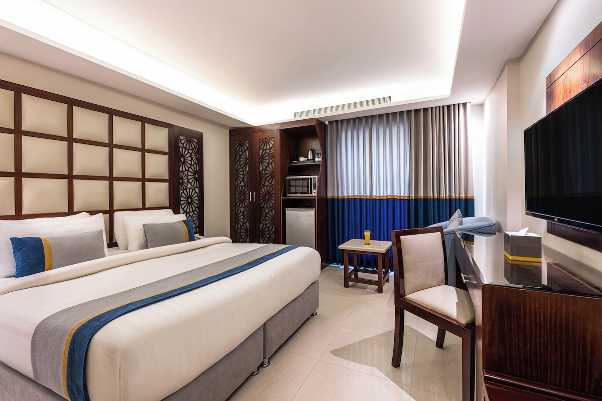 A hotel room with a large bed, a desk, a chair, a television, and a minibar.