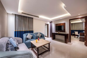 A modern hotel room with a sofa, a coffee table, a TV, and a desk.