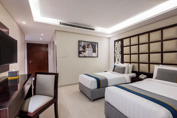 A hotel room with two beds, a desk, a chair, a TV, and a painting on the wall.