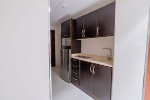 Cocina compacta con muebles oscuros, un refrigerador de acero inoxidable, un microondas y un lavaplatos con grifo.
