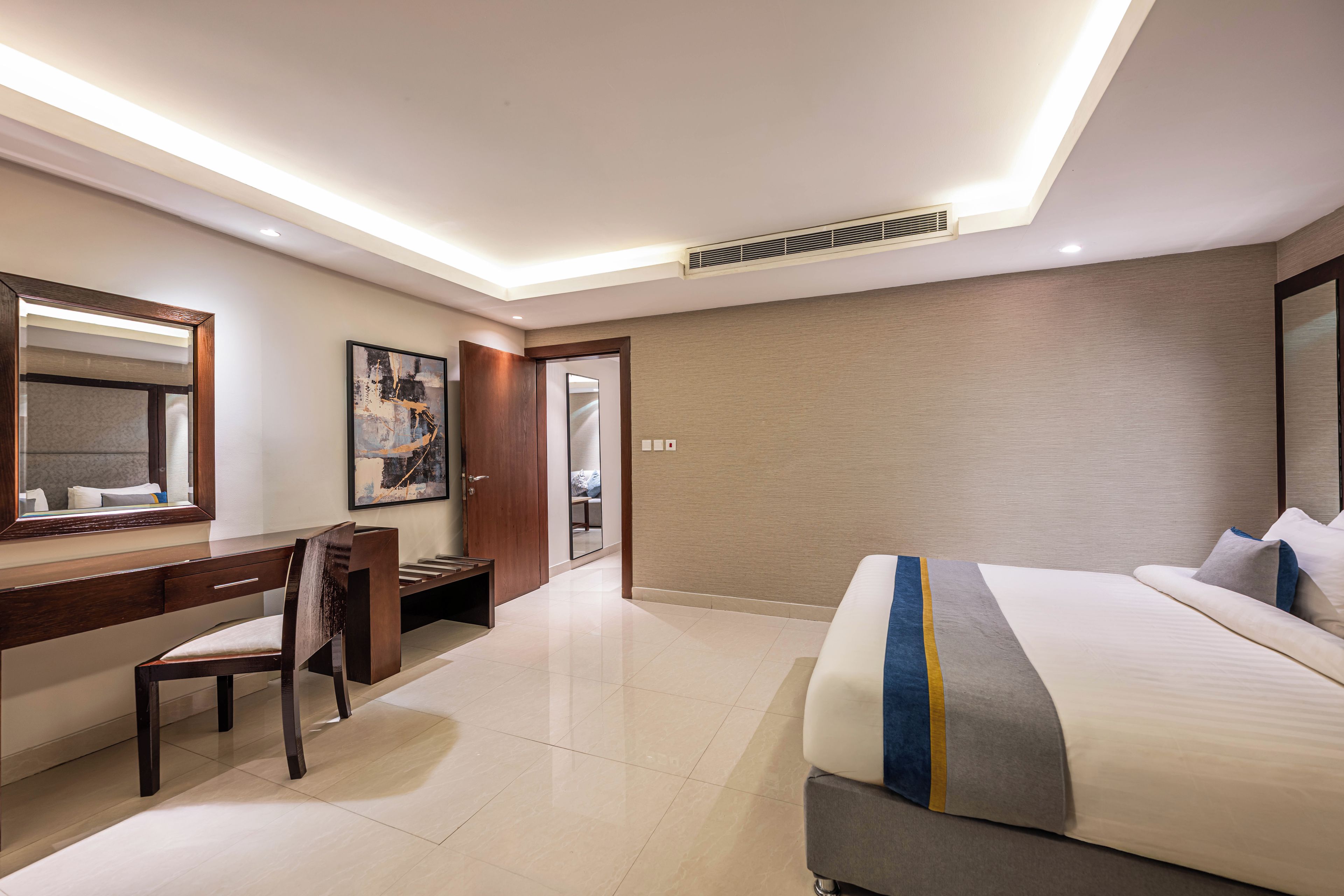 A hotel room with a bed, a desk, a chair, a large mirror, and a painting on the wall.