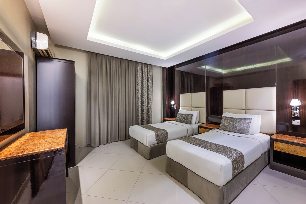 Habitación de hotel con dos camas, un espejo grande, un televisor y un diseño moderno en el techo.