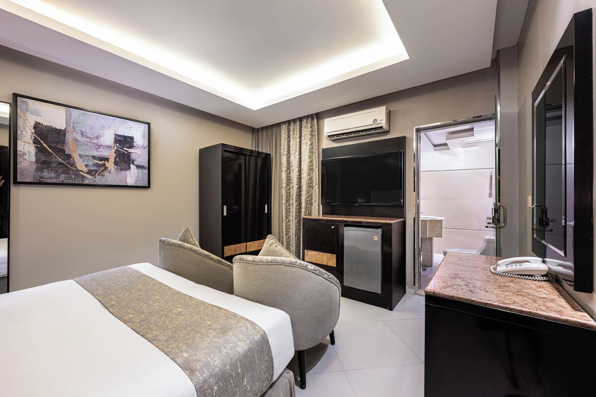 Habitación de hotel con dos camas, un escritorio con teléfono, televisor y aire acondicionado.