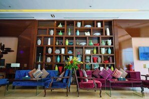 Eine Lobby mit einem blauen Sofa, einem violetten Sofa und einem Glastisch. Es gibt ein großes Holzregal, das mit verschiedenen Dekorationsobjekten gefüllt ist.