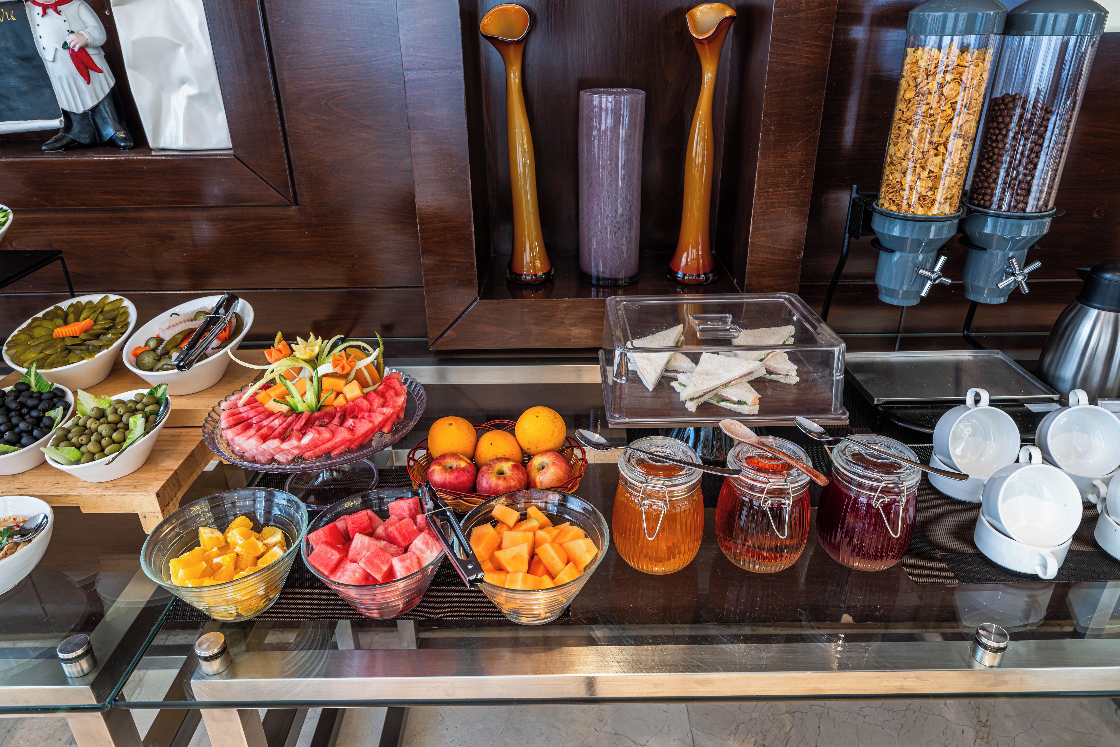 A buffet with various food items including fruits, sandwiches, and beverages.
