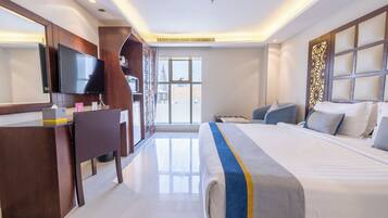 A hotel room with a bed, a desk, a television, and a view of the cityscape.