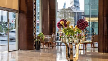 A modern interior with a glass table surrounded by chairs, a large window with a city view, and a decorative vase with flowers.
