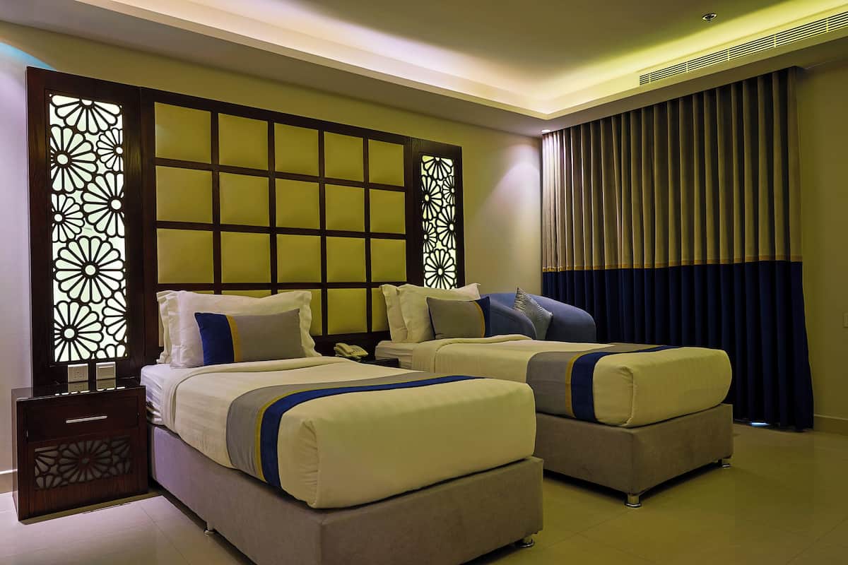 A hotel room with two beds, a decorative partition, a nightstand, and a large window with curtains.