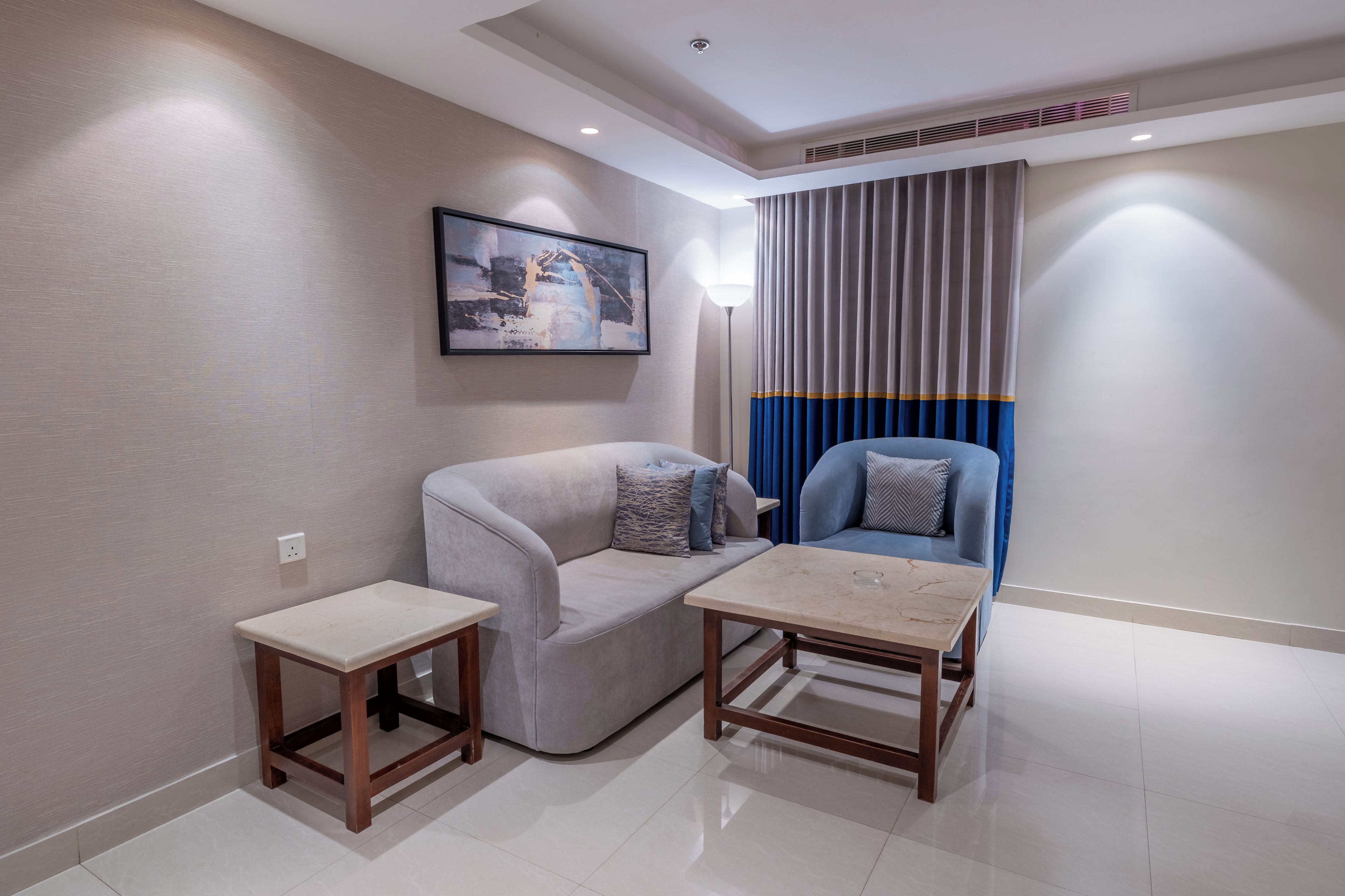 Un salon moderne avec un canapé gris, un fauteuil bleu, une petite table et un tableau accroché au mur.