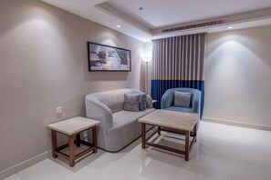 Una sala moderna con un sofá gris, un sillón azul, una mesita y un cuadro en la pared.