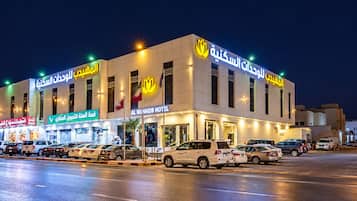 Un hôtel à plusieurs étages, un parking et plusieurs voitures garées devant.