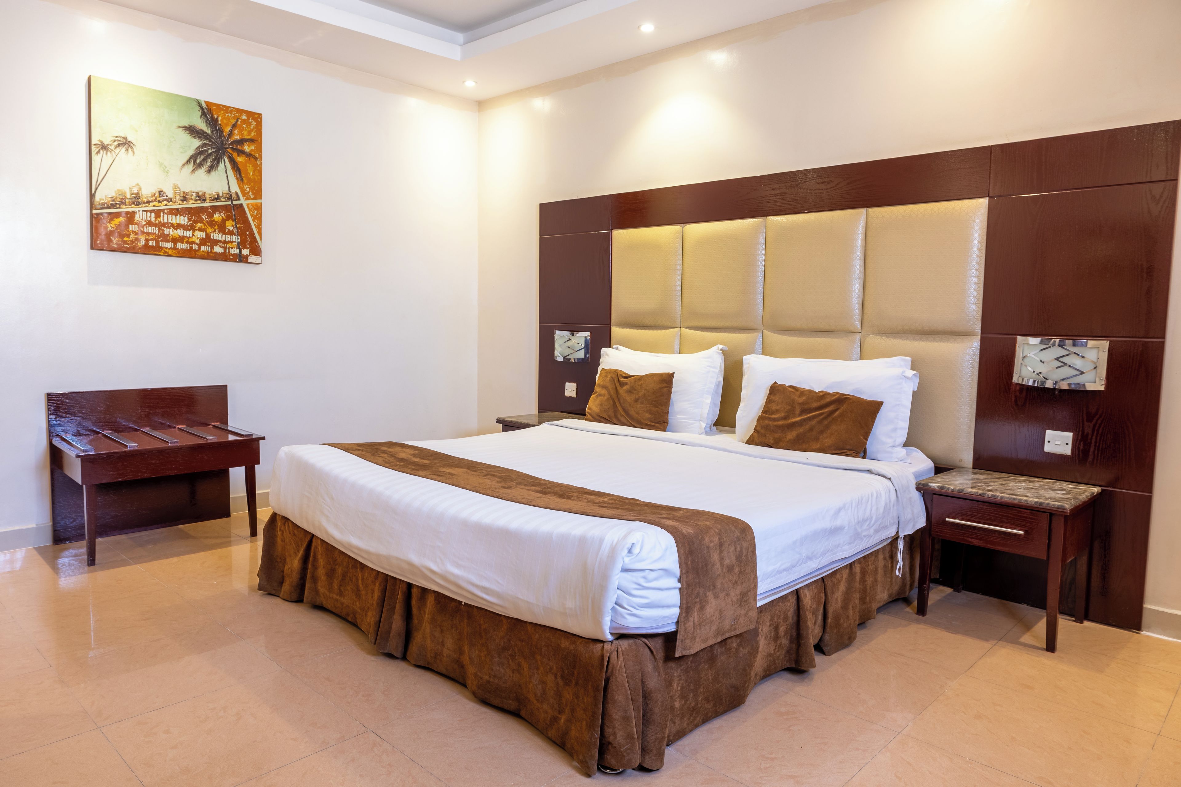 A hotel room with a large bed, a wooden bench, a nightstand, and a wall-mounted TV.