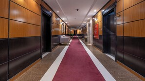 Un pasillo de hotel con alfombra roja, paneles de madera y una zona de estar central.
