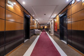 A hotel hallway with a red carpet, wooden panel walls, and a central seating area. - Al Muhaidb Residence Al Takhasossi 3 - Economic (Riyadh)