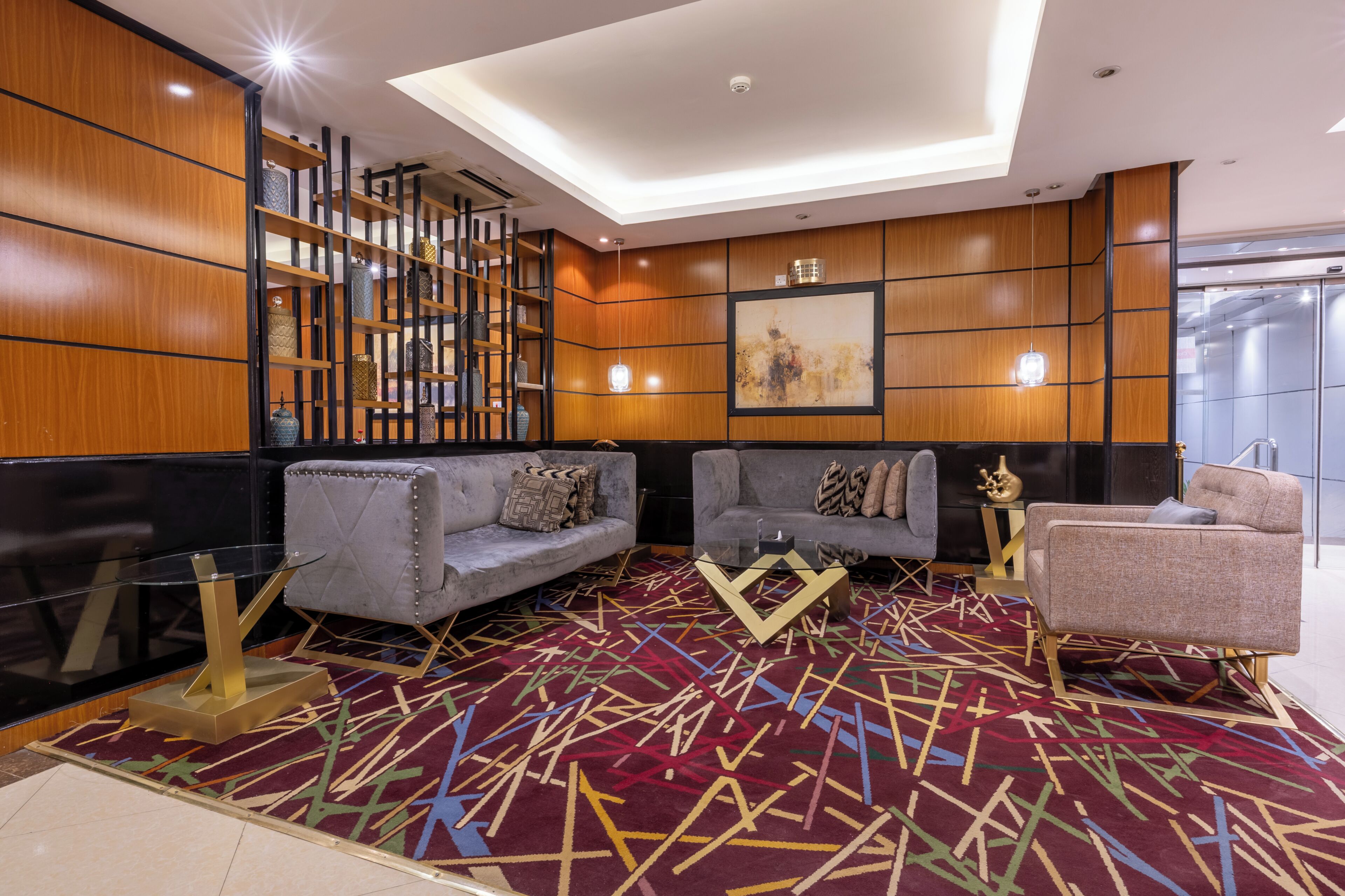 A modern lobby with a geometric patterned carpet, two sofas, a bookshelf, and a painting on the wall.