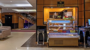Una cafetería con un mostrador exhibiendo bebidas y aperitivos, una escalera y un área de descanso con un sofá.