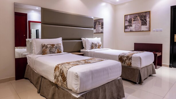 Ein Hotelzimmer mit zwei Betten, einem großen Spiegel, einem Gemälde und einer Tür.