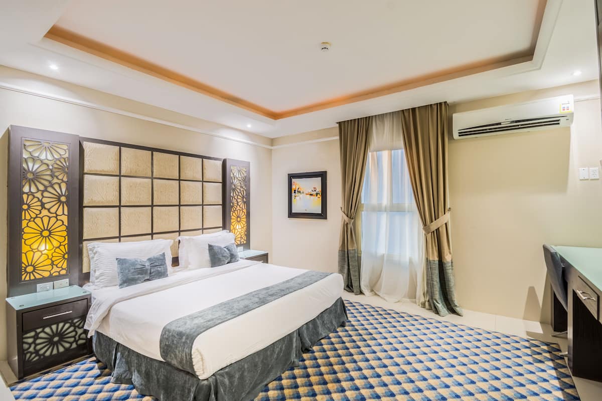 A hotel room with a large bed, a desk, and a window with curtains.