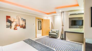 A hotel room with a bed, a desk with a flat-screen TV, a chair, and a bathroom with a mirror and sink.