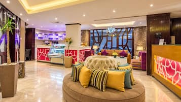A hotel lobby with a reception desk, a seating area with a tufted sofa, and a decorative wall.