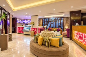 A hotel lobby with a reception desk, a seating area with a tufted sofa, and a decorative wall.