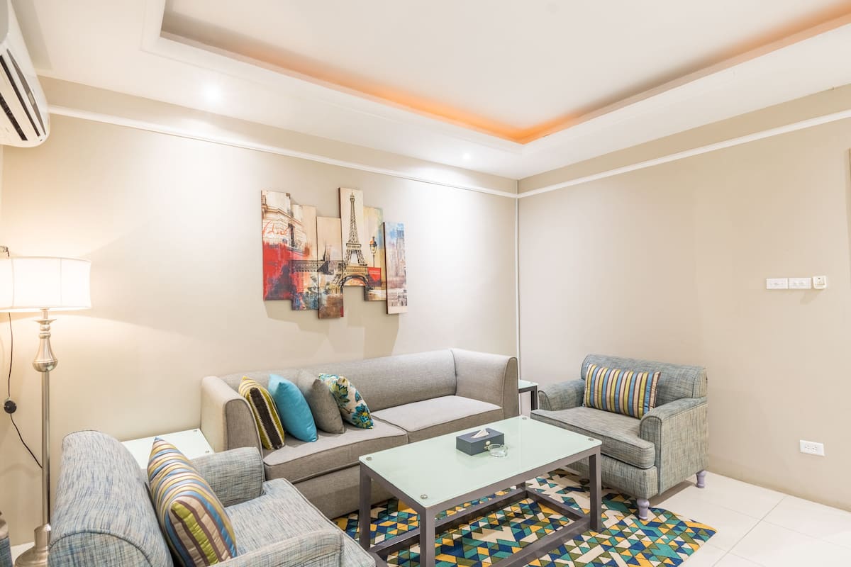 A modern living room with a sofa, armchairs, a coffee table, and a patterned rug.