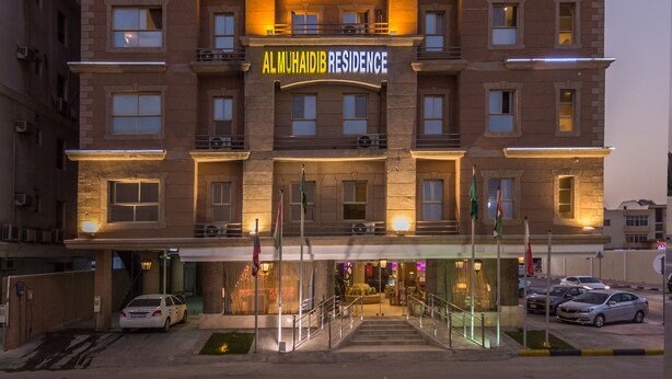 Un hôtel à plusieurs étages, doté d’une enseigne bien visible indiquant « Al Muhaiyib Residence » et d’une inscription en arabe au-dessus.