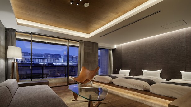 Ein modernes Hotelzimmer mit Blick auf die Stadt, einem Glastisch, einem Ledersessel und zwei Betten.