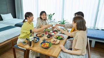 A group of people dining at a wooden table in a hotel room with a bed and curtains in the background.