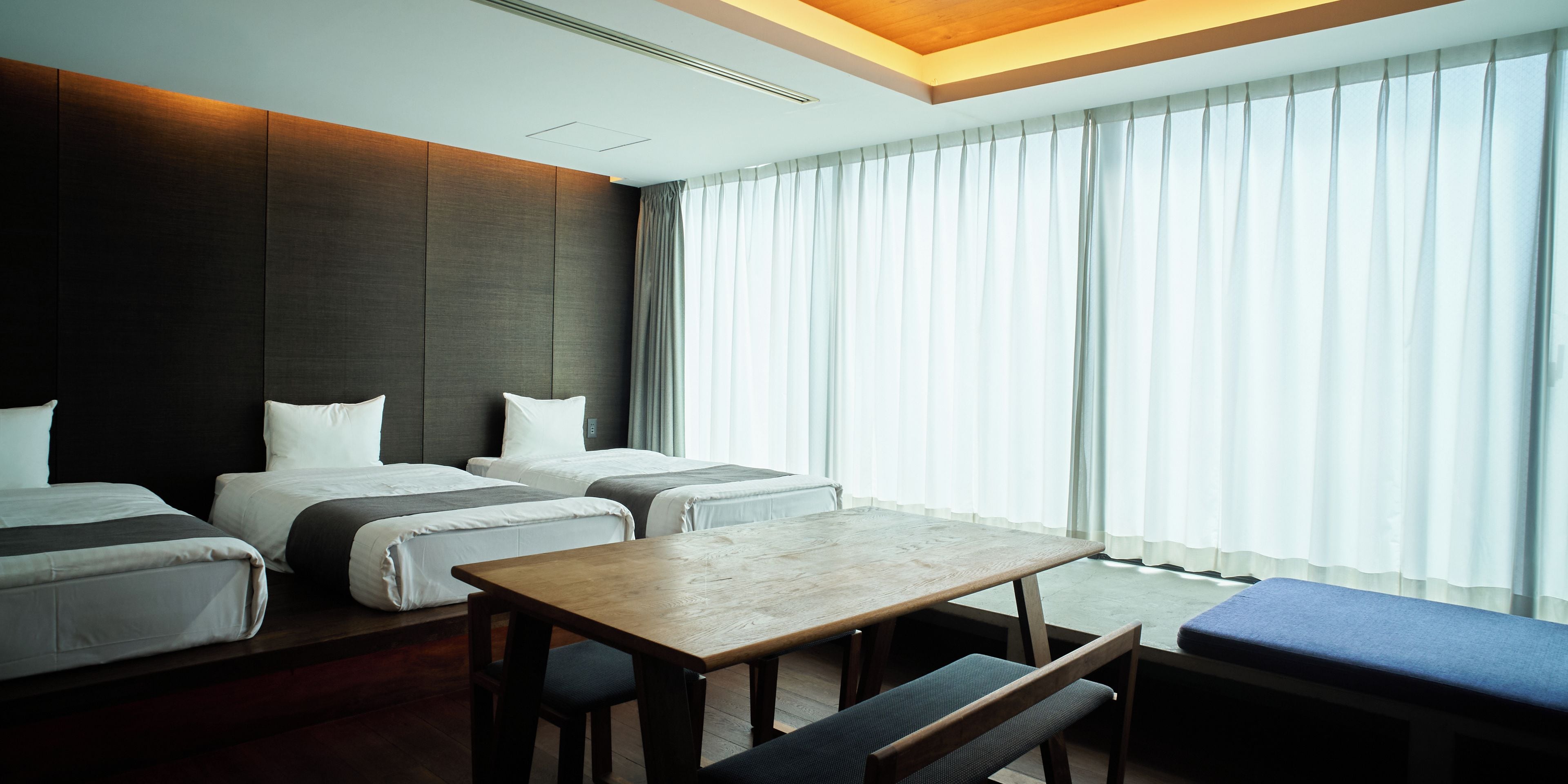 A hotel room with a large bed, a smaller bed, a desk, and a bench.