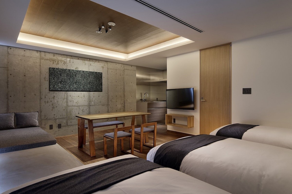 A modern hotel room with a wooden ceiling, a dining area, a TV, and a sofa.