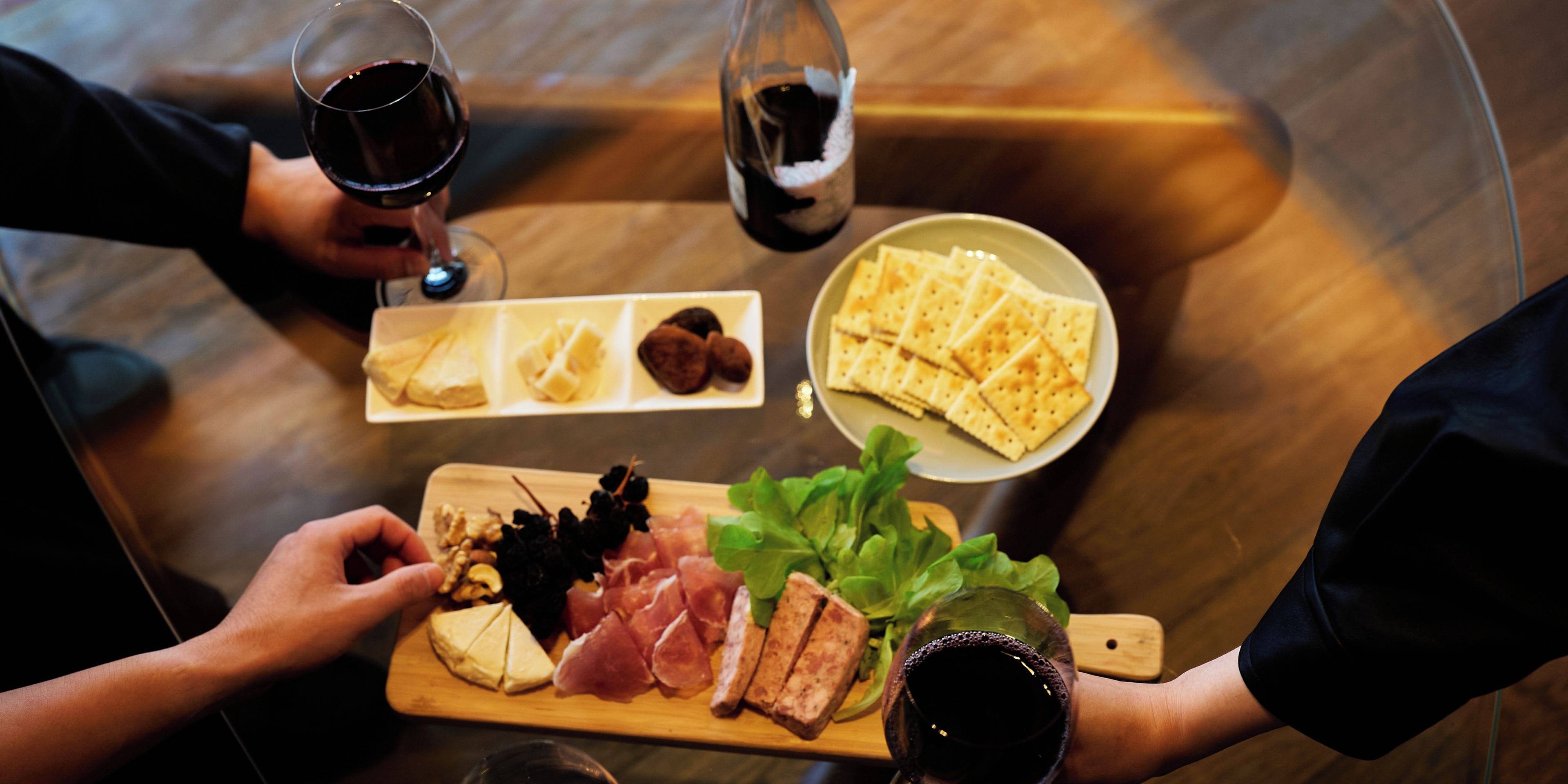 A table with a variety of food items, including cheese, meats, and crackers, along with glasses of wine.