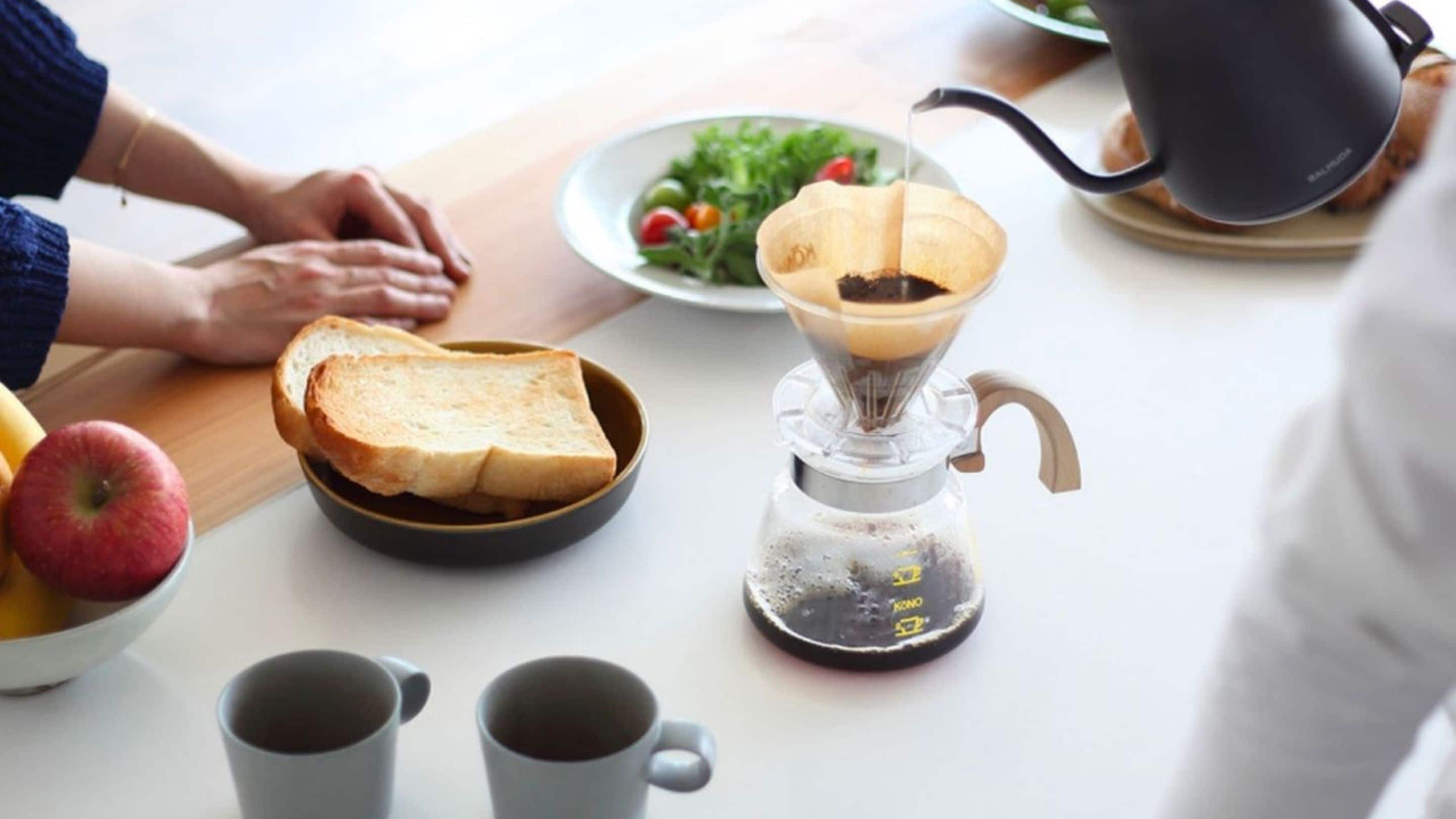 Eine Küchenarbeitsplatte mit Kaffeemaschine, Toast in einer Schüssel, einem Salat Teller und einer Obstschale.