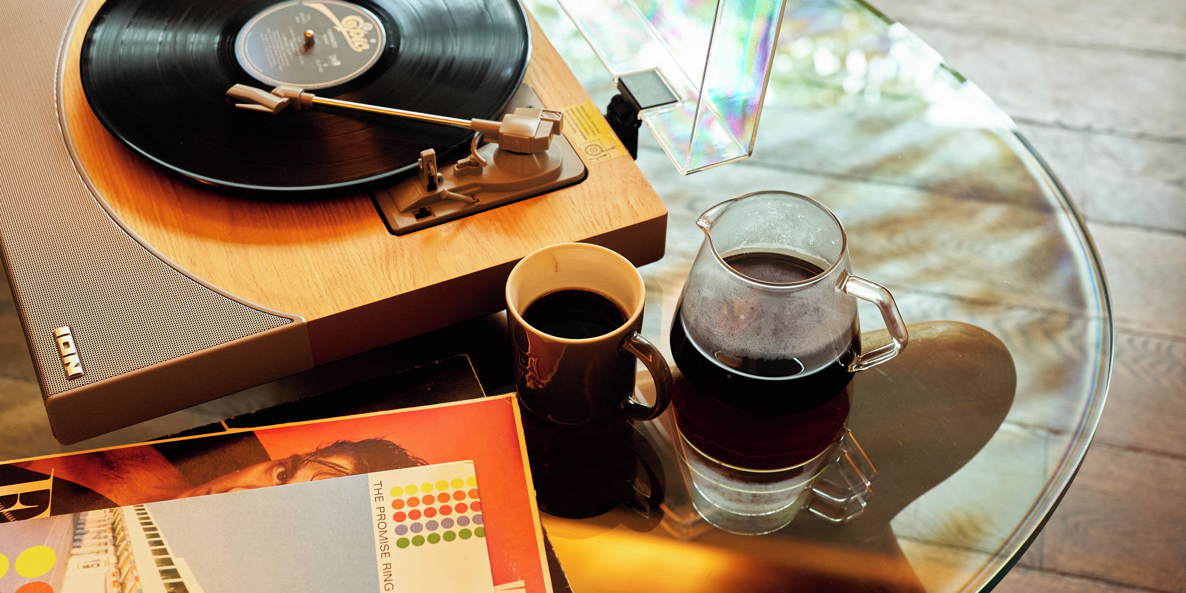 A vinyl record player, a mug, and a glass of tea on a glass table.