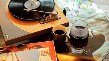 A vinyl record player, a mug, and a glass of tea on a glass table.
