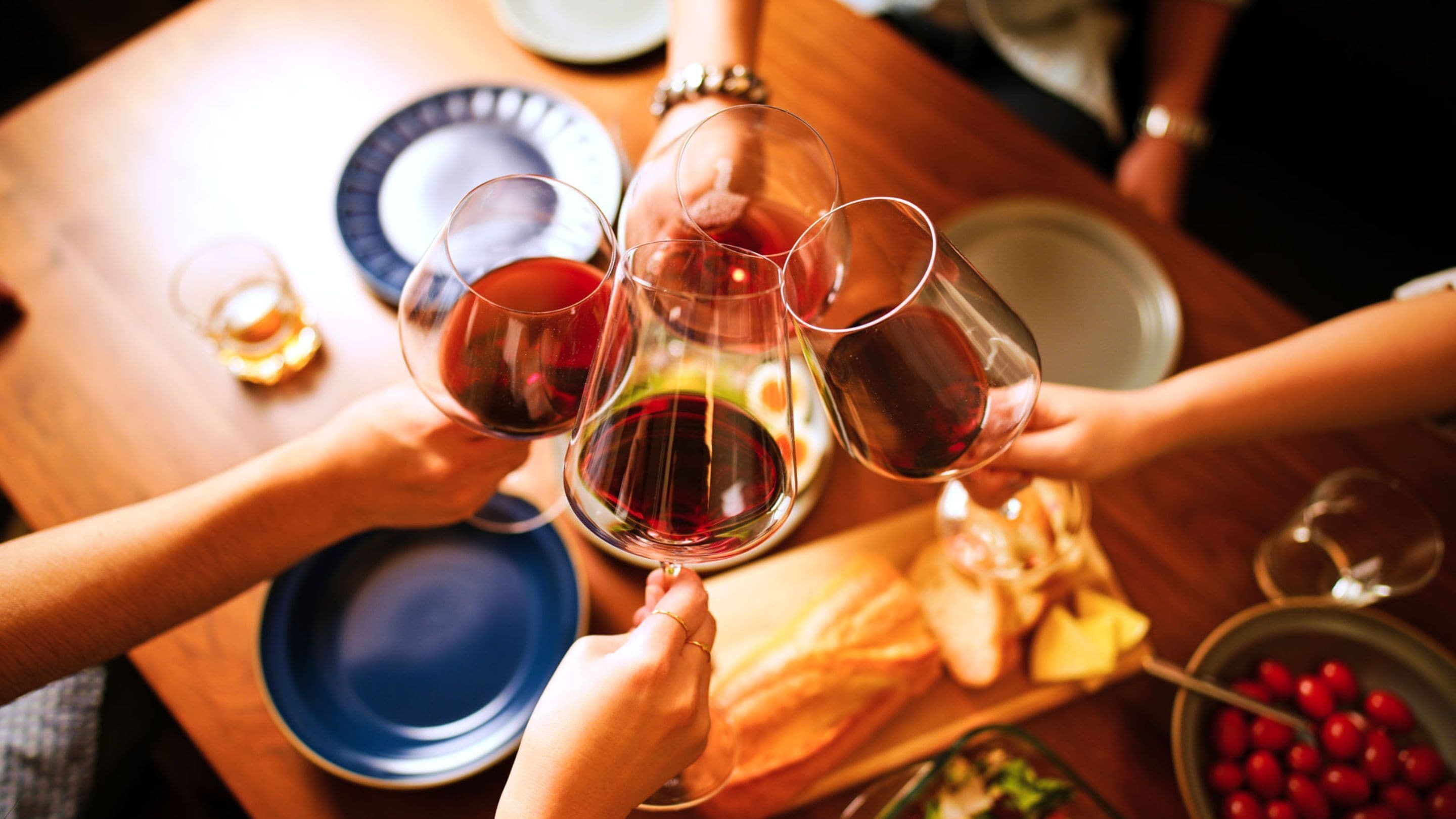 A group of people toasting with wine glasses around a wooden table with plates and food.