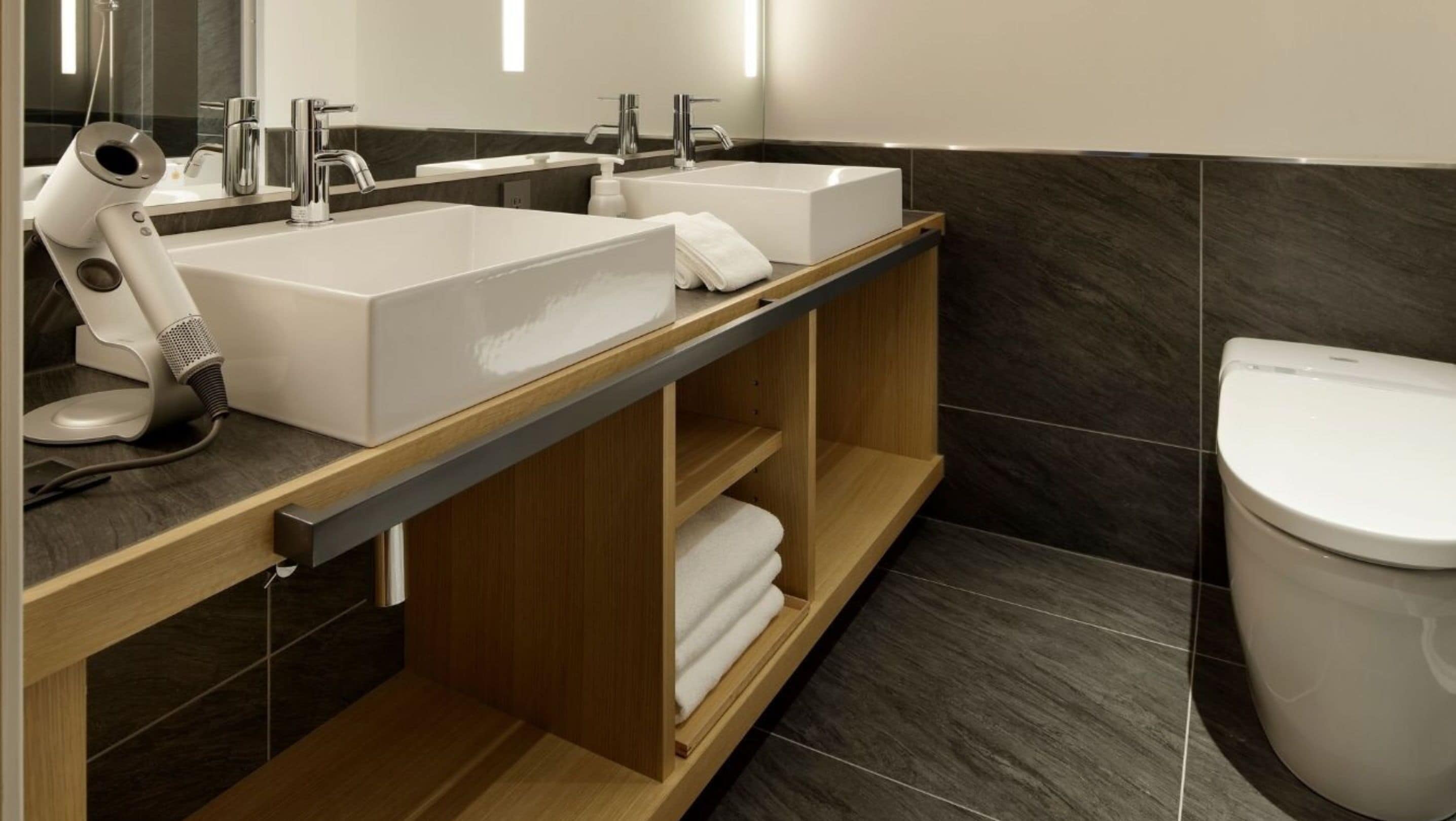 A modern bathroom with two sinks, a hairdryer, and a toilet.