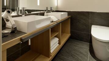 A modern bathroom with two sinks, a hairdryer, and a toilet.
